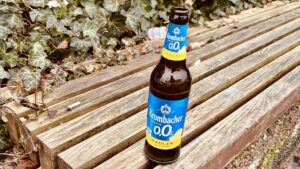 Alles falsch - Eine Krombacher 0,0% Radler Bierflasche steht auf einer Holzbank, mit Efeu und Laub im Hintergrund.