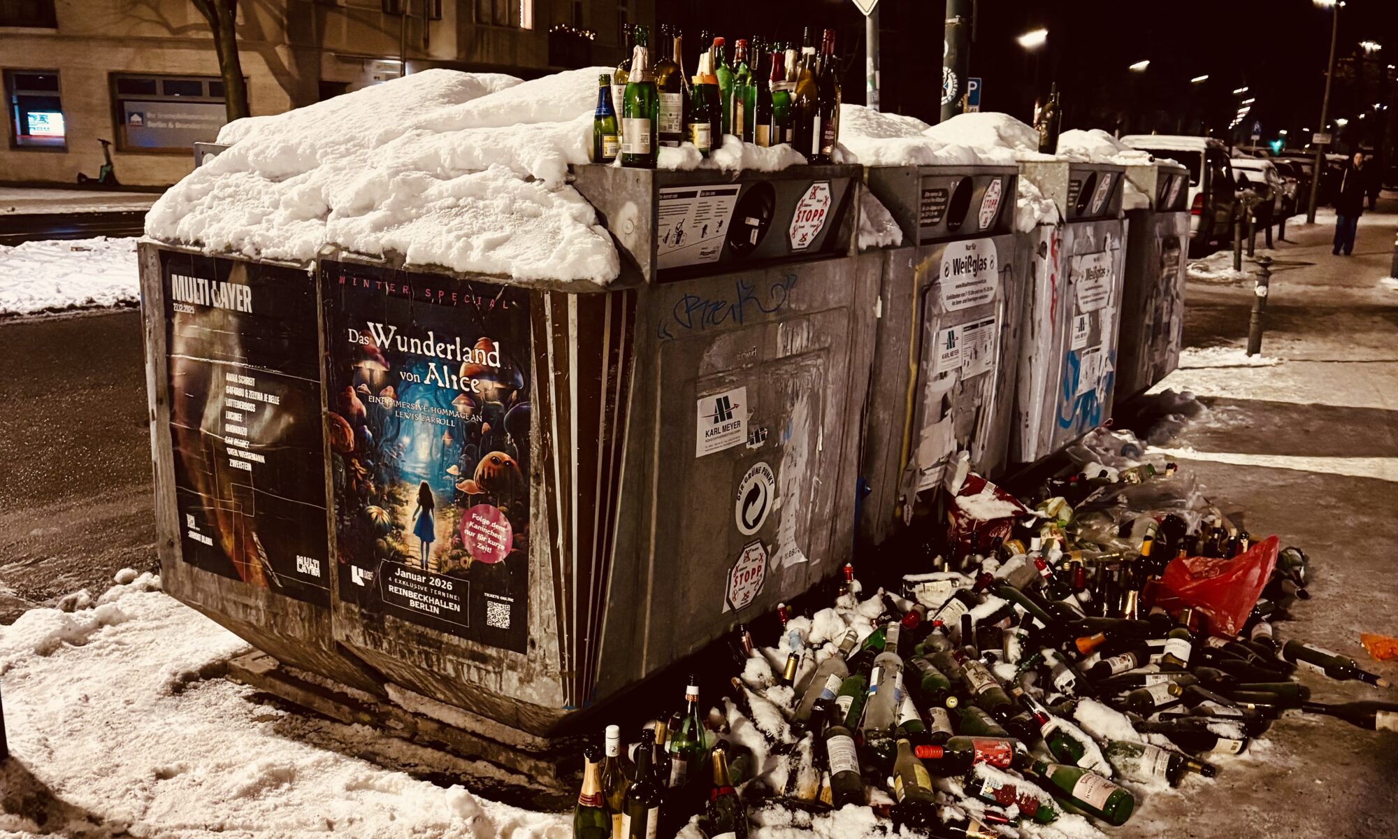 Flaschen, Fragen und Antworten - Eine nächtliche Straßenszene mit schneebedeckten Metallrecyclingcontainern, die mit weggeworfenen Glasflaschen überlaufen und mit Schnee bedeckt sind, beleuchtet von Straßenlaternen.