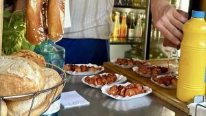 Wochenrueckblick kw 27 2026 tdc tour de currywurst - Gegrillte Würstchen in Papierbooten, auf die eine Hand Soße träufelt, daneben ein Brotkorb, aufgehängte Brezeln und eine große Senfflasche an einem Essensstand.